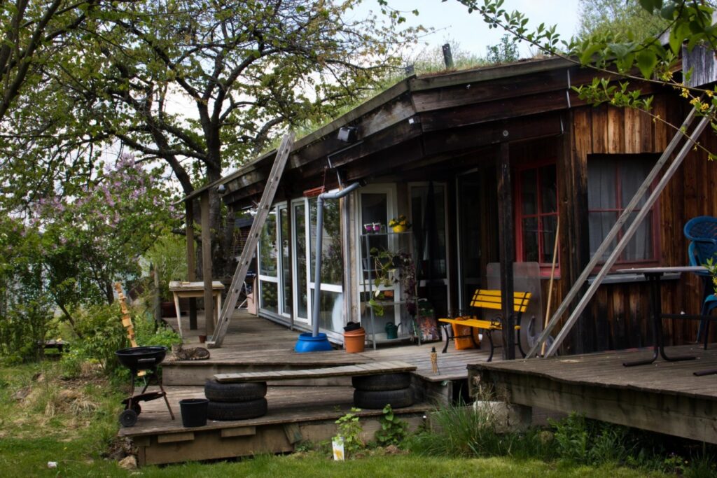 Außenaufnahme der Terrasse einiger Zimmer im Südgarten. Eine Holzbaureihe an Zimmer mit Bäumen am linken Bildrand