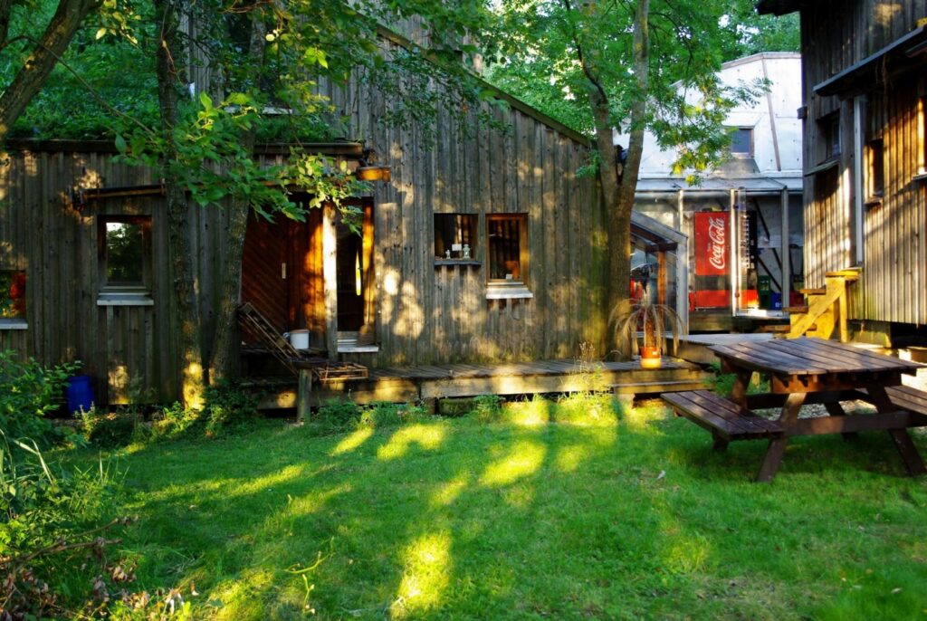 Foto der Holbau-Konstruktion der Mühle aus dem Nordgarten. Fassade eines winkeligen Holzbaus mit einer grünen Wiese im Vordergrund