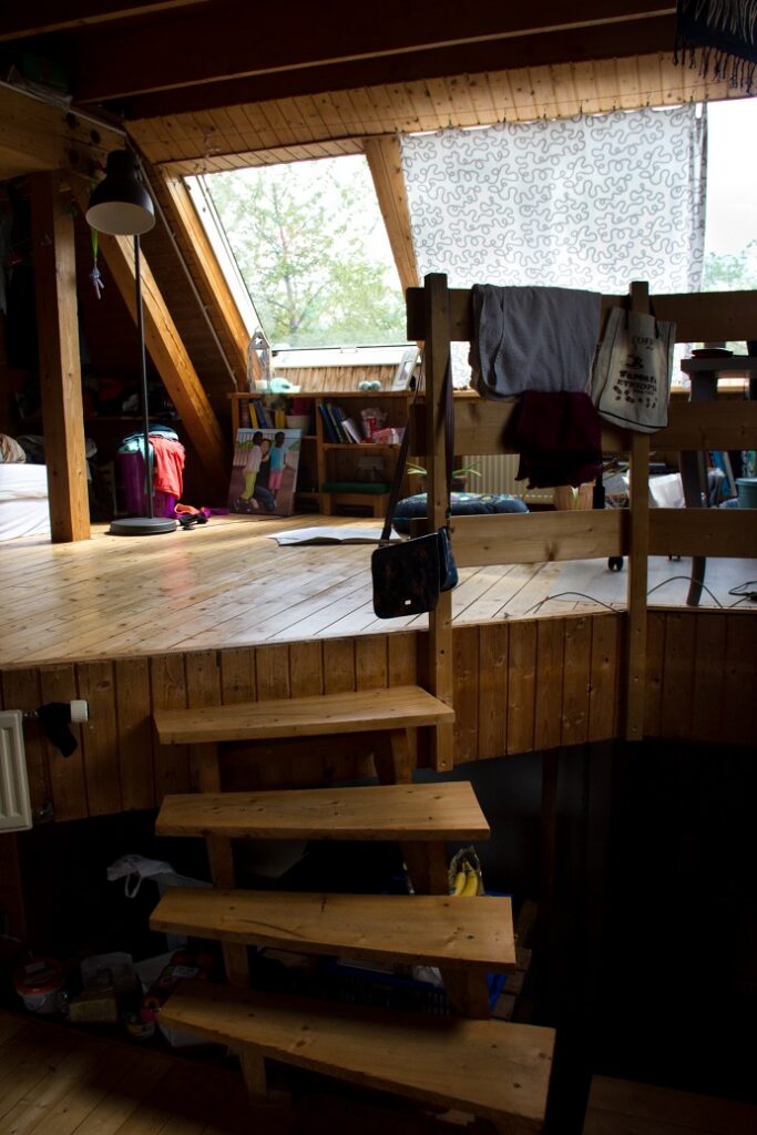 Foto aus einem Zimmer. eine kleine Holztreppe führt zu einer höheren Ebene mit große Schrägdach-Fenster. Der gesamte Bau ist aus Holz