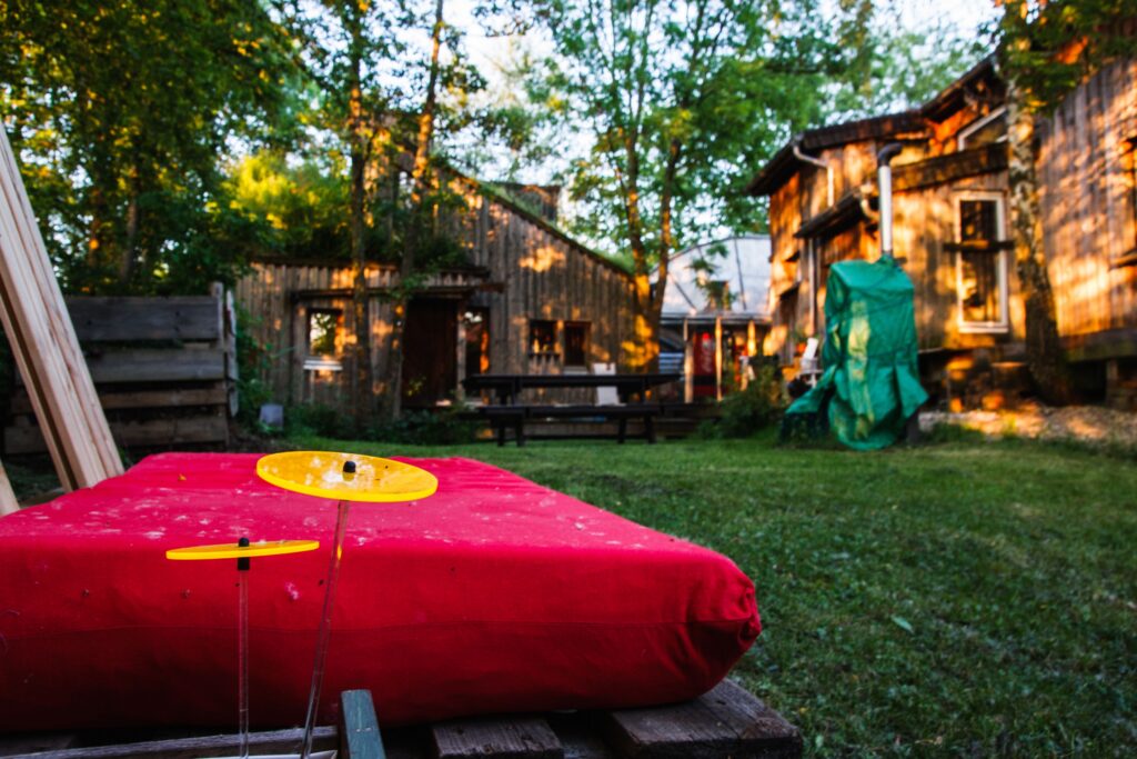 Nahaufnahme einer roten Sitzfläche im Nordgarten. Im Hintergrund leicht verschwommen der verwinkelte Holzbau des Häusles mit einer grünen Wiese und Bäumen